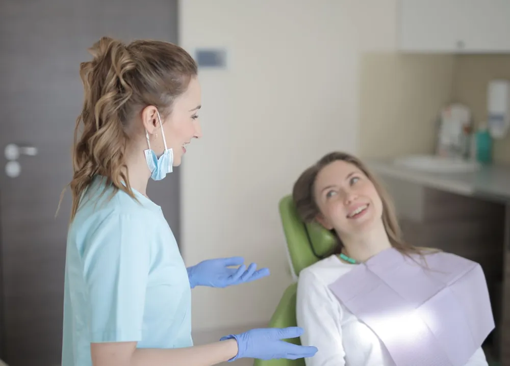 A hygienist in light blue scrubs chatting with a relaxed patient before her check-up