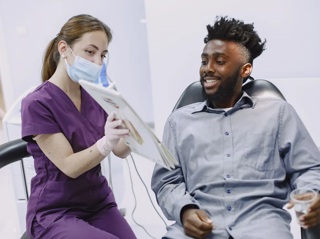 A patient smiling in the treatment chair while a hygienist shows him his plan on a tablet