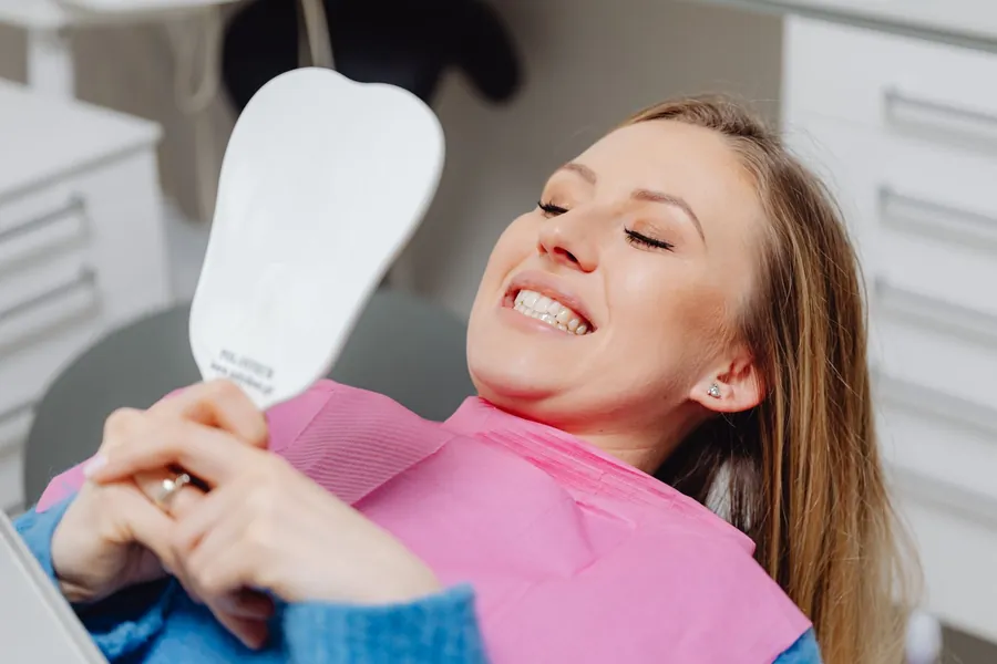 A woman laughing in the dental chair as she looks at her smile in a hand mirror