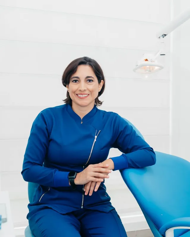 Dr. Elena Navarro in blue scrubs, smiling, seated beside a treatment chair