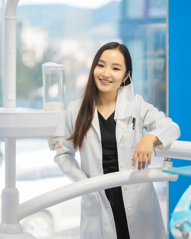 Dr. Hannah Cho in a white coat, leaning on a treatment chair and smiling