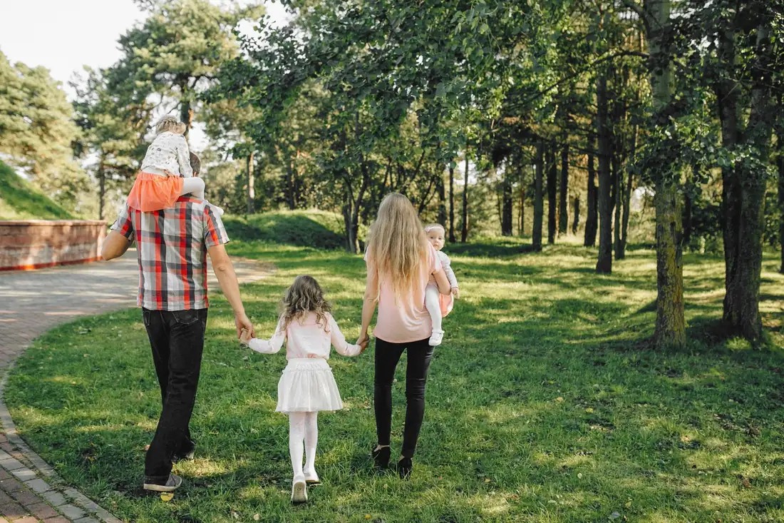A family of two parents and three small children walking away along a sunlit park path