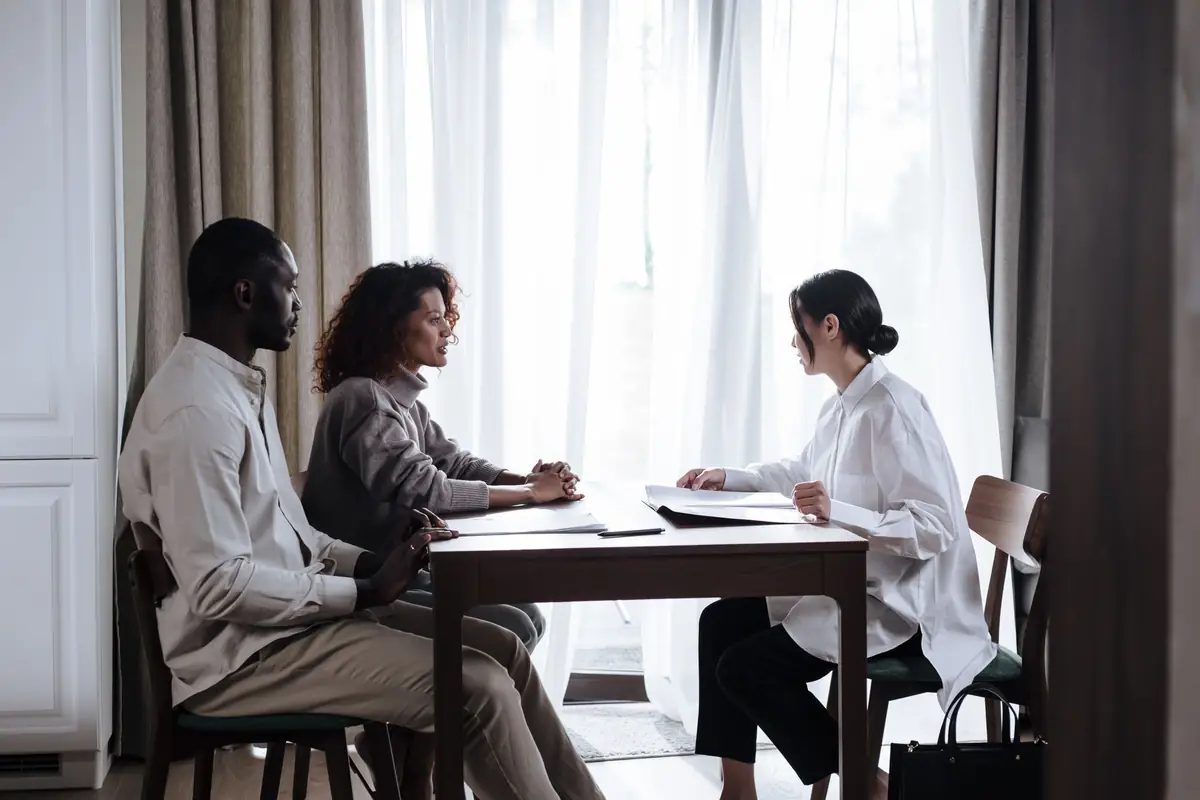 Two clients and an attorney talking across a wooden table beside sheer curtains