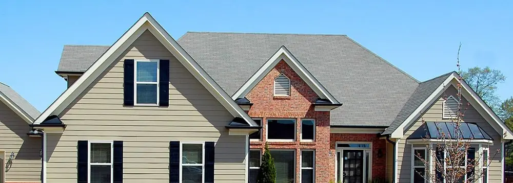 Gray shingle roof on a tan-sided home with a red brick entry