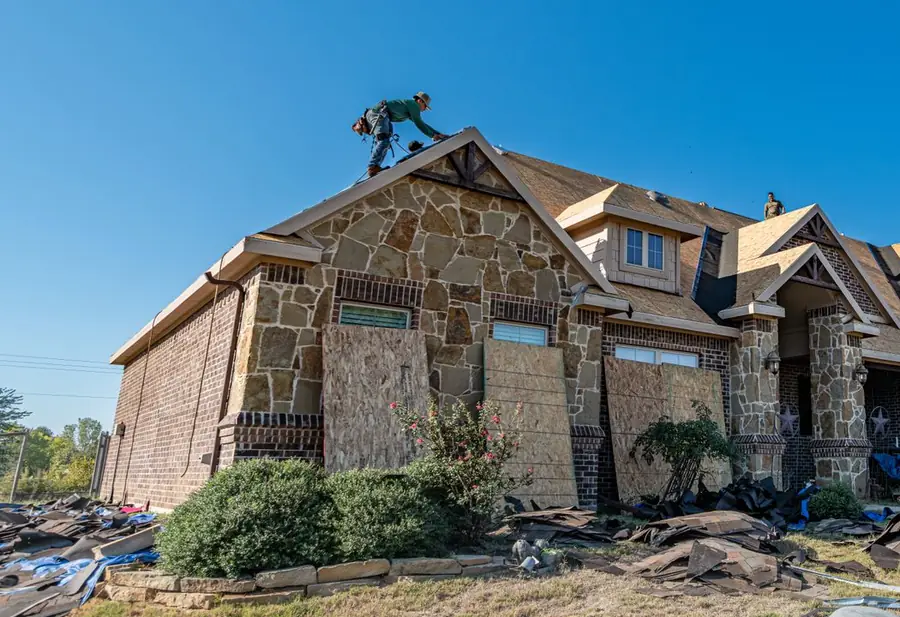 Crew replacing the roof on a stone and brick home, with the windows boarded for the job