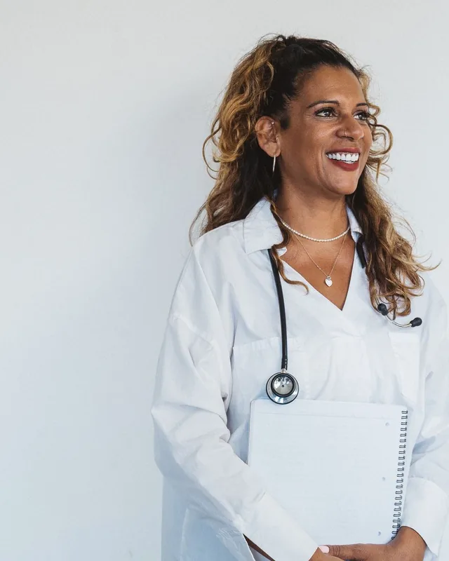 Camille Reyes, registered nurse and injector, smiling in a white coat and holding a notebook
