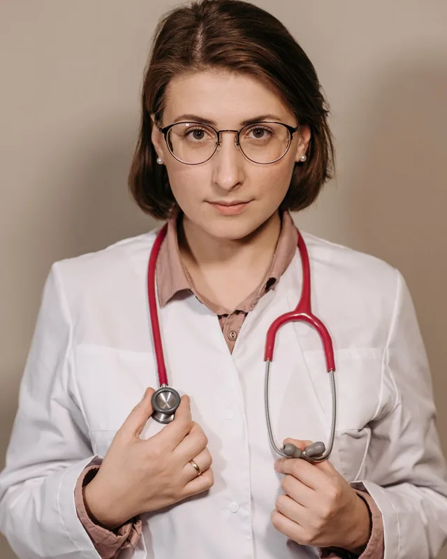 Natalie Brandt, nurse practitioner, in a white coat with a stethoscope against a warm neutral wall