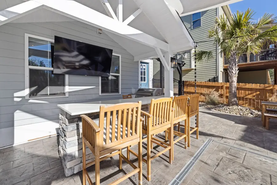 Covered outdoor kitchen with a stone-veneer bar, wooden bar stools and stamped patterned paving