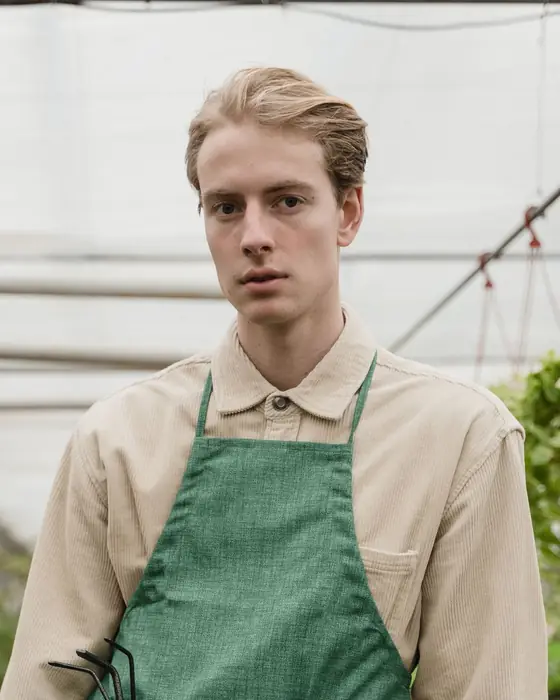 Owen Pruitt, horticulturist, in a green apron inside a greenhouse