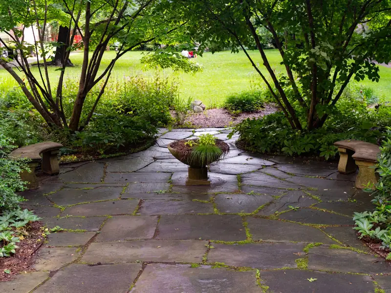 Irregular bluestone courtyard with a planted stone urn and two curved benches under multi-stem trees