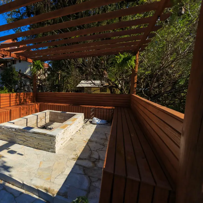 Cedar pergola over built-in benches and a stacked-stone fire box on a flagstone floor